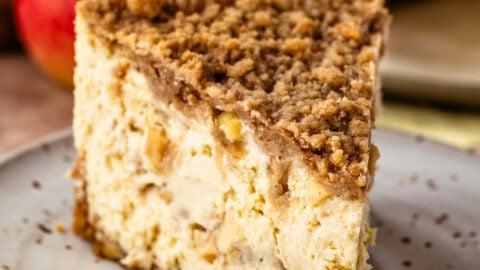 Close-up shot of the layers of an apple crumble cheesecake, highlighting the creamy cheesecake, apple filling, and crumble topping
