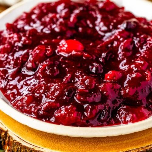 Rustic Thanksgiving spread with a prominent bowl of homemade cranberry sauce, garnished with fresh herbs.