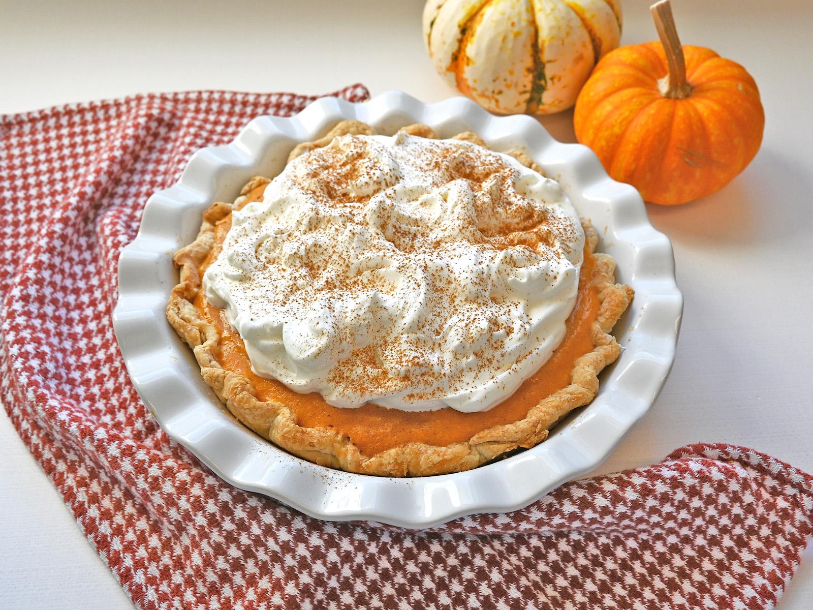 Homemade pumpkin pie with a decadent whipped cream swirl, garnished with a sprinkle of cinnamon, cozy autumn setting