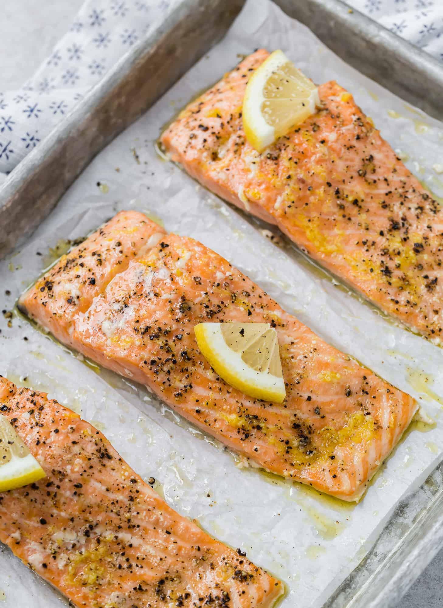 fresh salmon fillets being seasoned with chopped herbs and lemon zest on a baking sheet