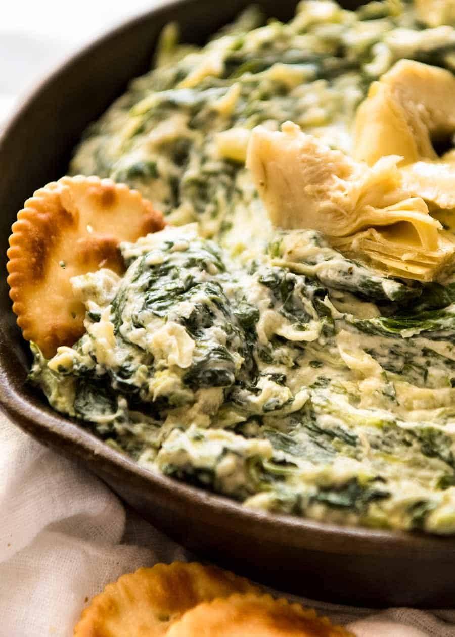 Delicious creamy spinach artichoke dip with crusty bread and vegetable dippers on a rustic table