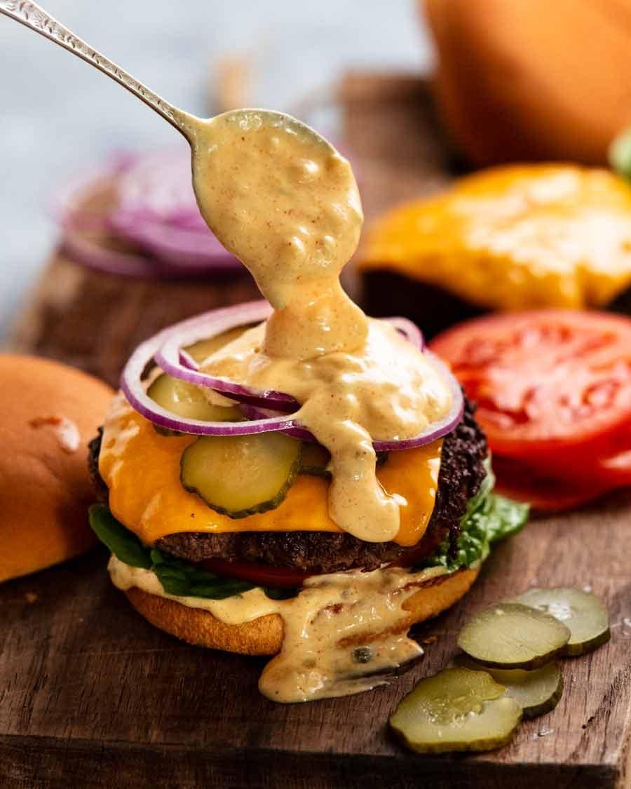 Bowl of creamy secret burger sauce with ingredients like pickles and spices around it