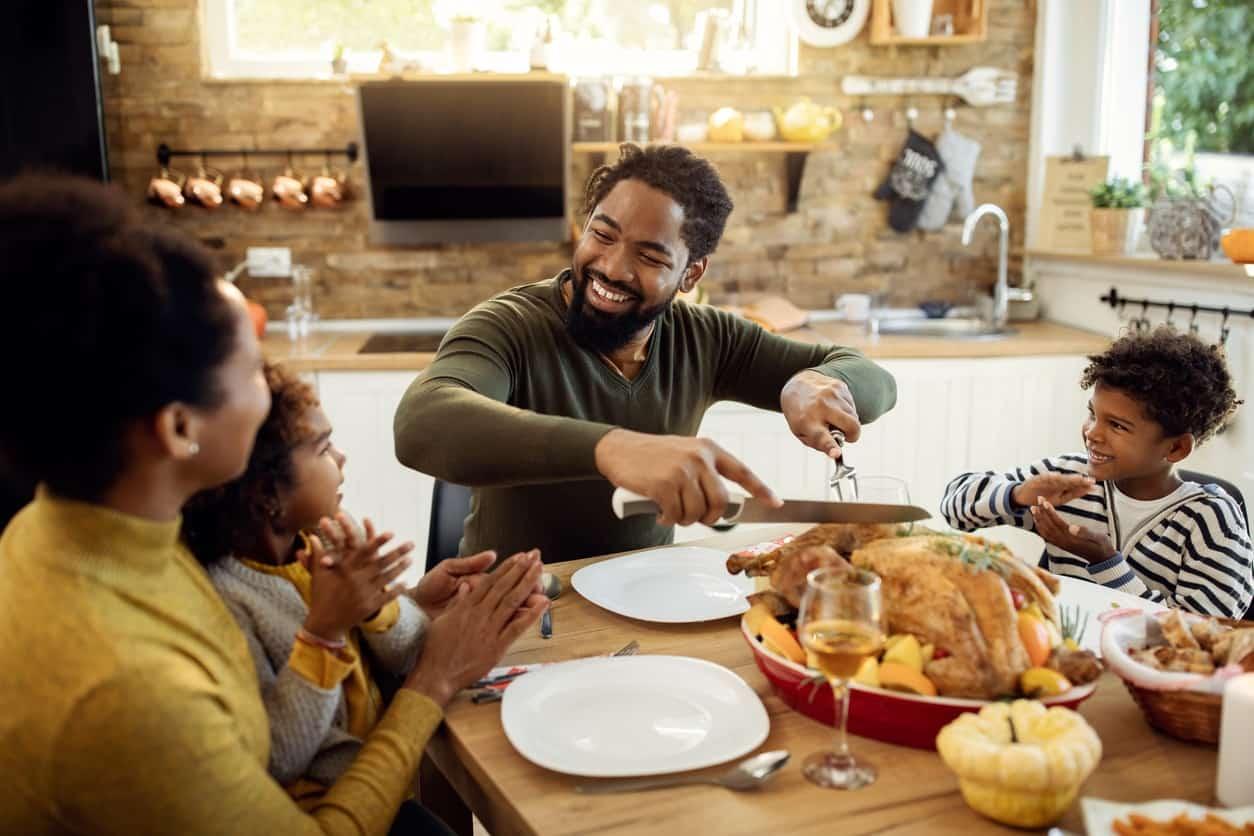 Person smiling while carving a perfectly roasted turkey, family gathered around a dining table