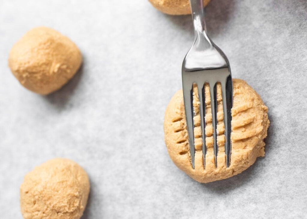 vintage-style photo of hands pressing a fork into peanut butter cookie dough on a baking sheet