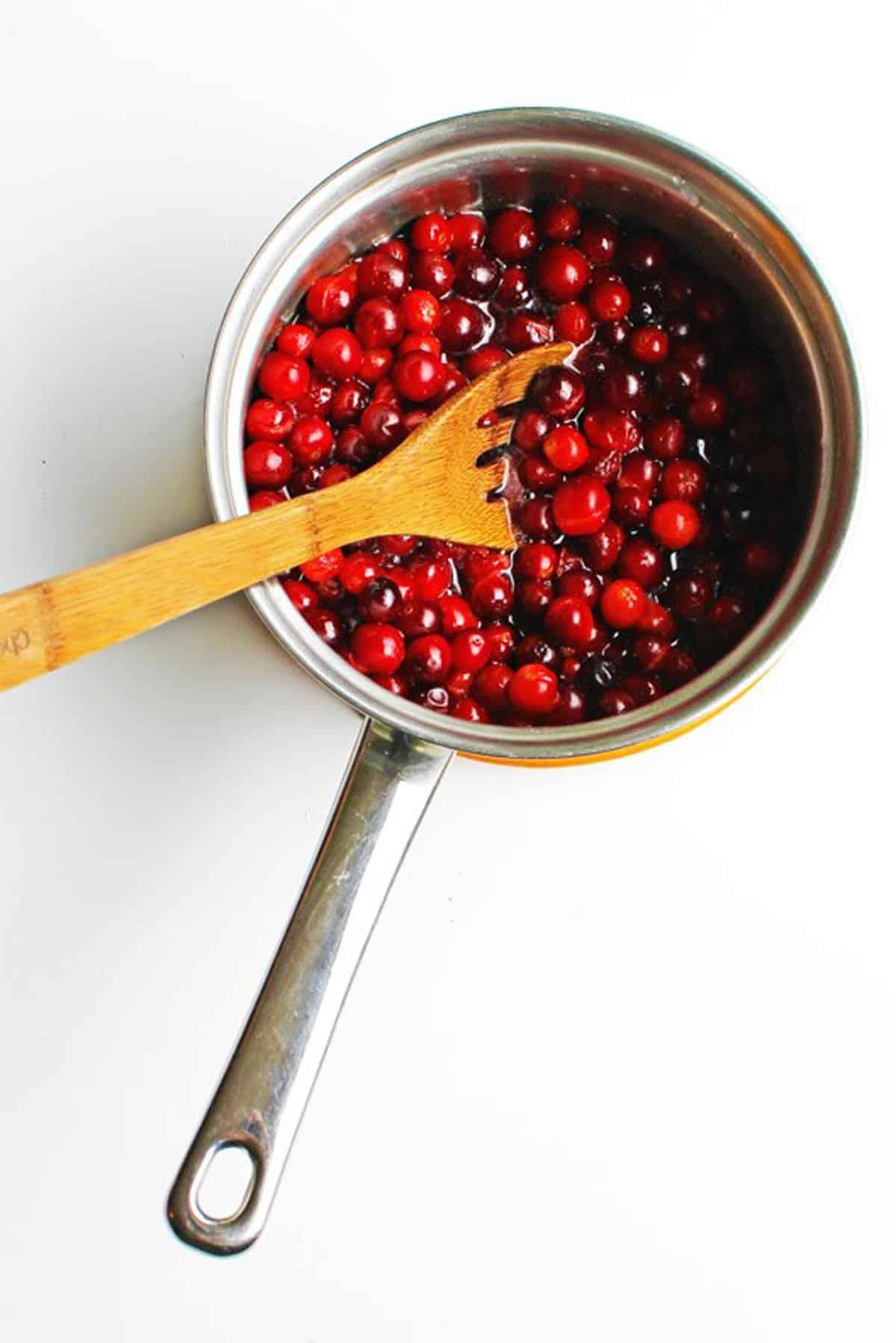 overhead shot of a saucepan simmering whole berry cranberry sauce with steam rising