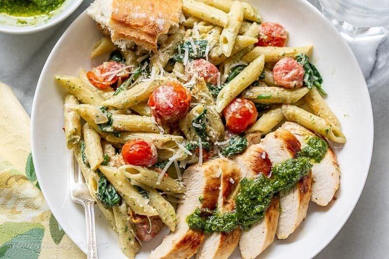 overhead view of creamy pesto chicken served with a side of pasta and cherry tomatoes