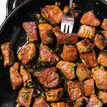 steak bites sizzling in garlic butter in a cast iron skillet