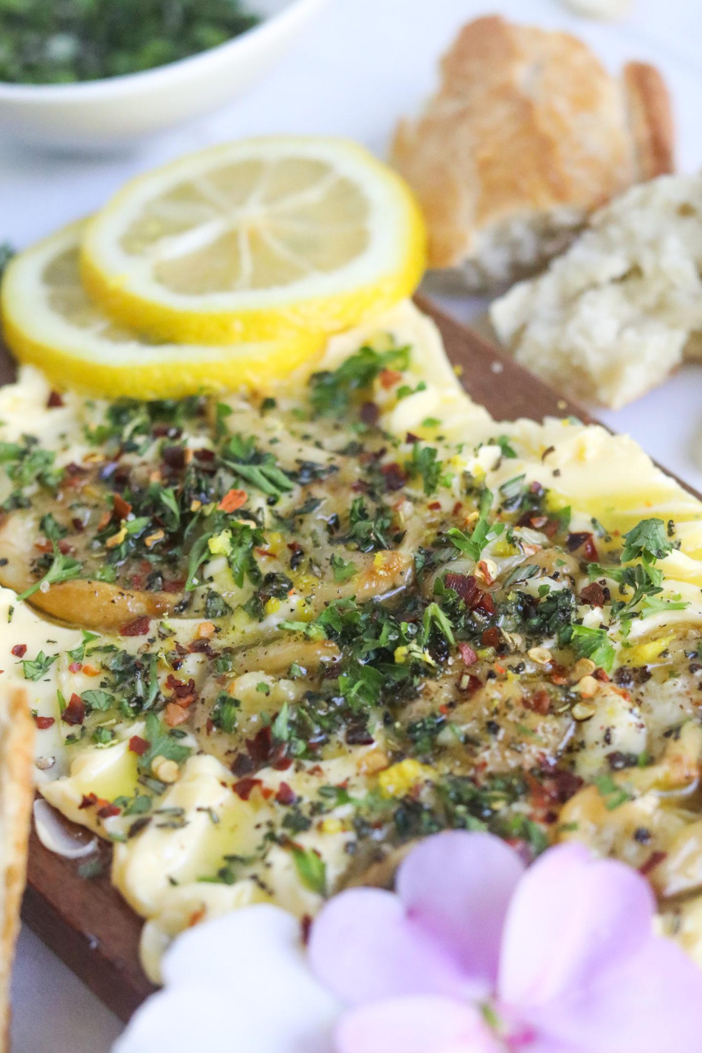 Close-up of fresh rosemary sprigs, garlic cloves, and lemon slices next to a stick of butter