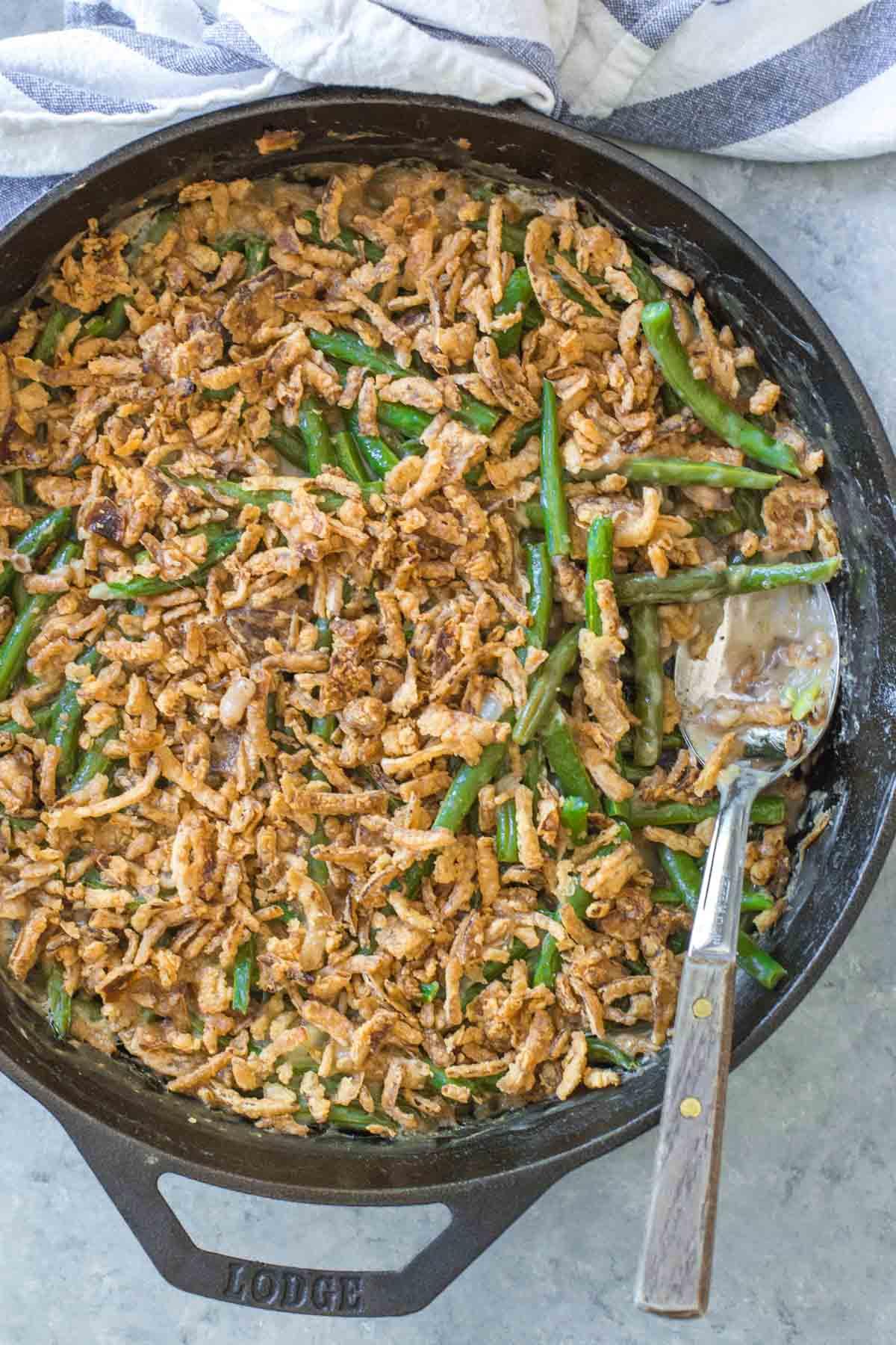 overhead shot of a full green bean casserole dish on a wooden table with serving spoon