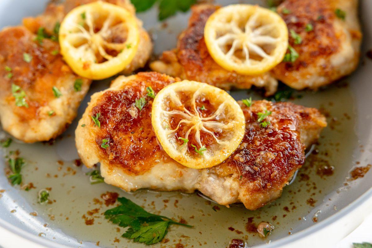close-up shot of golden brown chicken thighs in a skillet with lemon slices and herbs