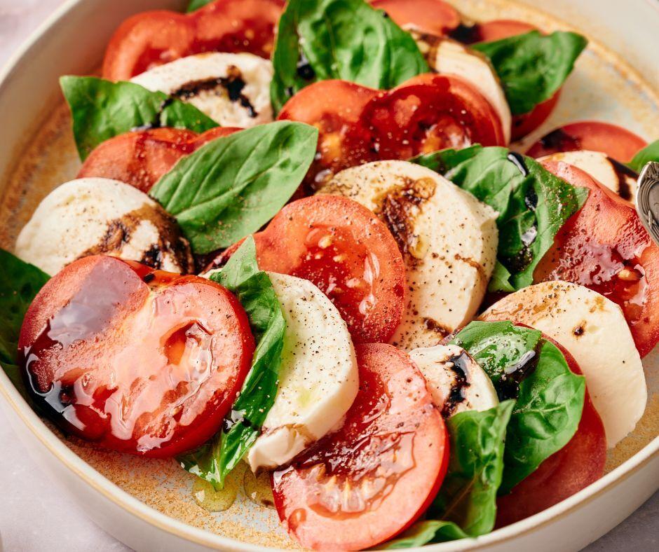 Several small bowls of Caprese Sorbet, each garnished with a basil leaf and a swirl of balsamic glaze, arranged on a rustic wooden table
