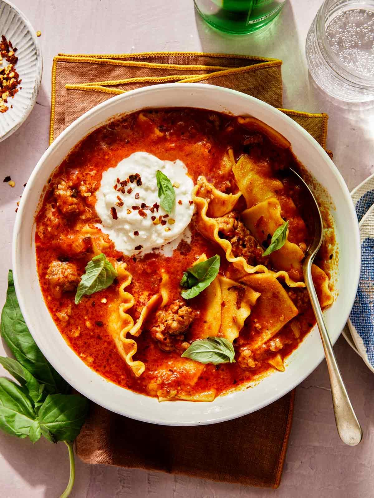 close up of a spoon scooping lasagna soup with cheese pull and fresh basil garnish