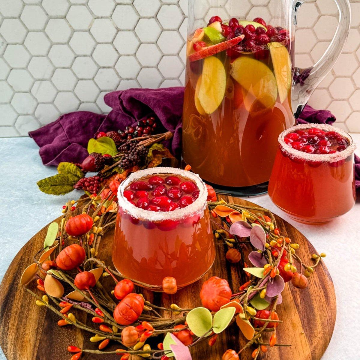 Overhead shot of a punch bowl filled with Friendsgiving Cinnamon Punch, surrounded by mugs and fall foliage