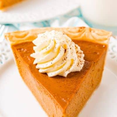 Close-up of a slice of vanilla pumpkin pie on a white plate with a fork, showing its soft texture and creamy filling