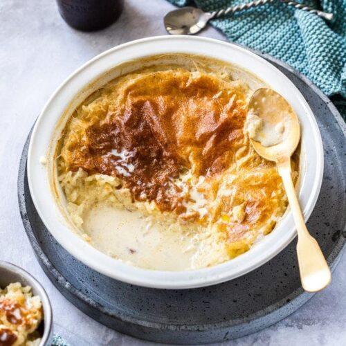 Close-up of a steaming bowl of baked rice pudding, with a vintage spoon resting on the side, soft focus background