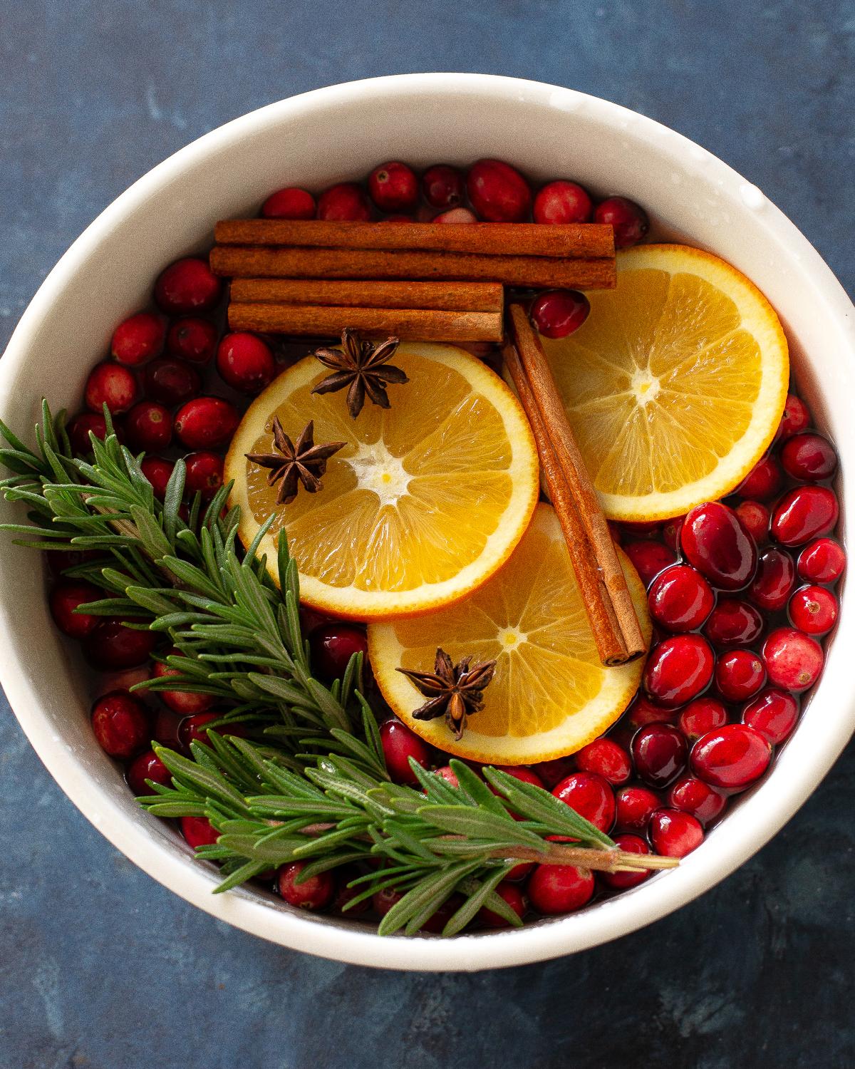 Rustic Christmas simmer pot with oranges, cinnamon, star anise, cloves, and cranberries, steam rising, warm lighting