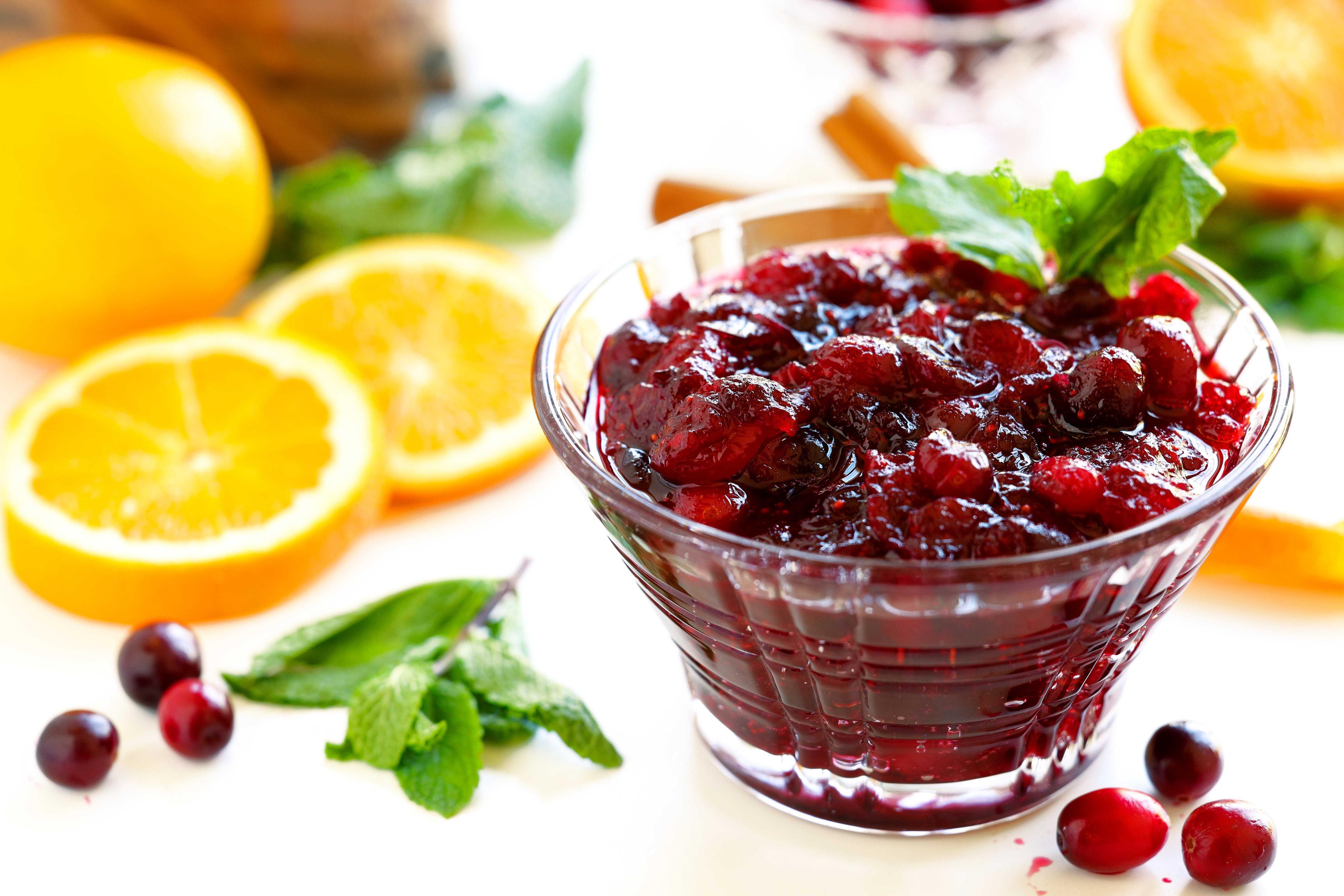 Homemade cranberry sauce cooling in a glass jar, garnished with an orange slice