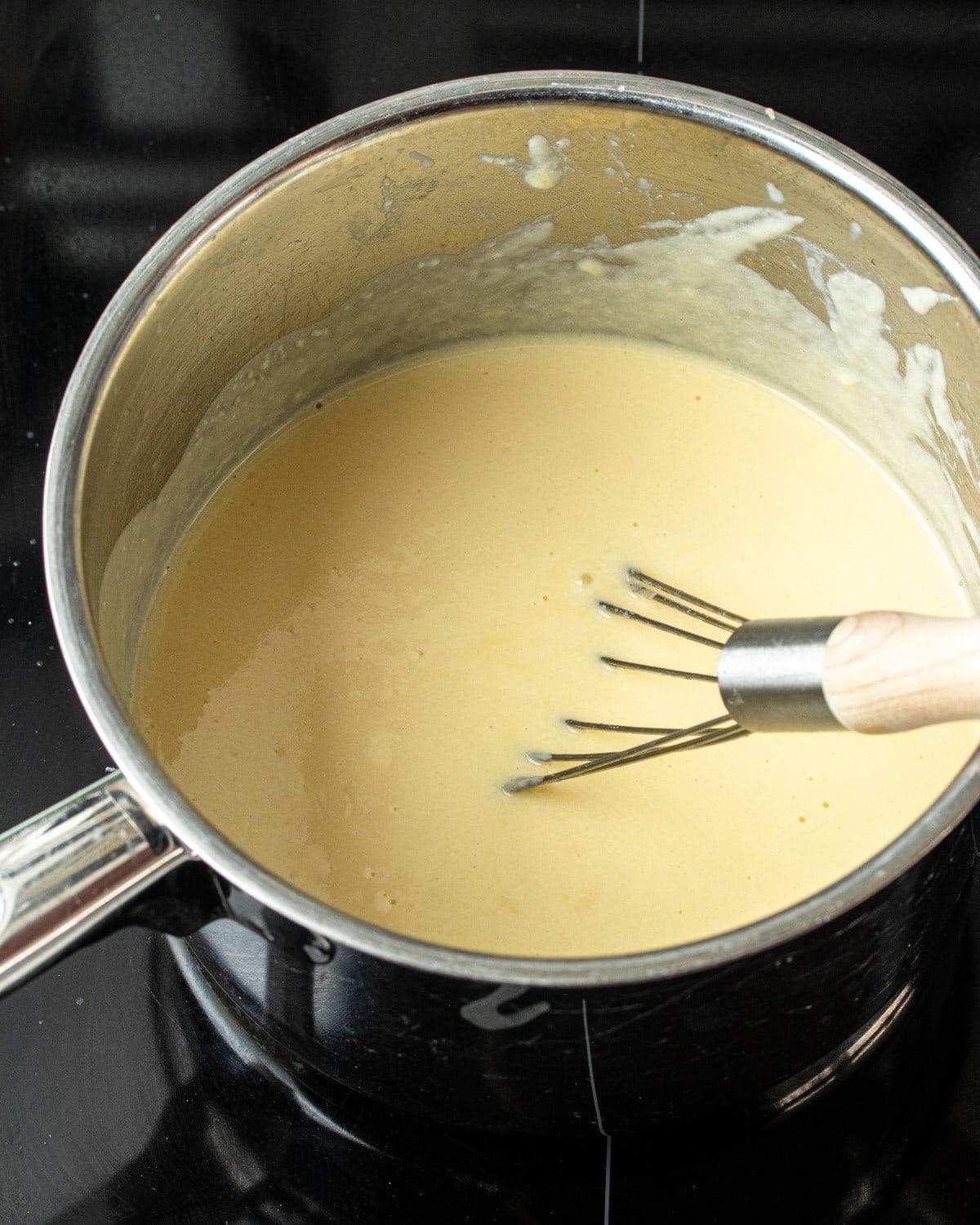 hands whisking a cheese sauce in a saucepan