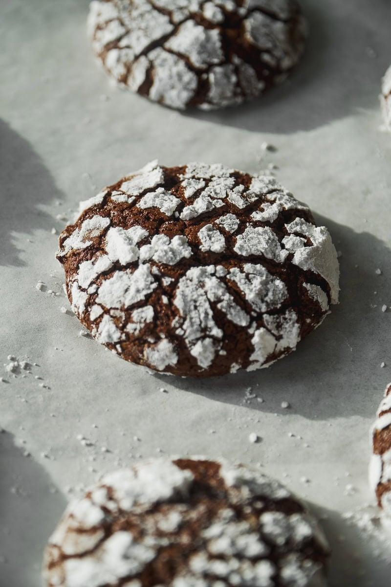 Plate of freshly baked chocolate crinkle cookies, steam gently rising, with a cozy, festive background