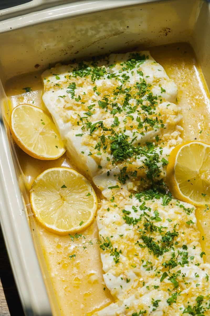 Beautifully golden baked cod fillet with fresh lemon slices and parsley garnish on a white plate, close-up, healthy dinner