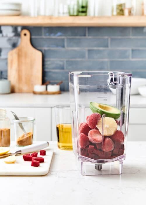 overhead shot of a blender with ingredients for the Berry Thyme Treasure Smoothie scattered around it on a wooden countertop