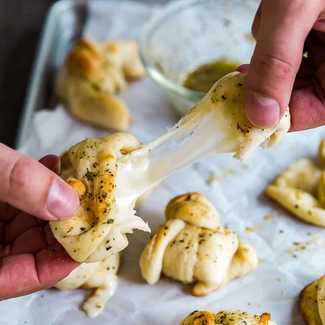 Close-up of a hand pulling apart a warm cheesy garlic knot, showing the melted mozzarella stretch