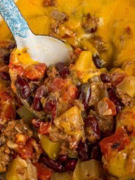 Close-up shot of a spoon scooping a portion of Cowboy Casserole, showing layers of beef, corn, and creamy potato topping