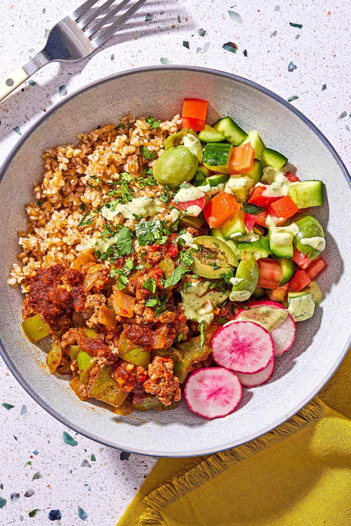 Overhead shot of fresh herbs, smoked paprika, and ground beef being mixed in a large bowl, vibrant colors