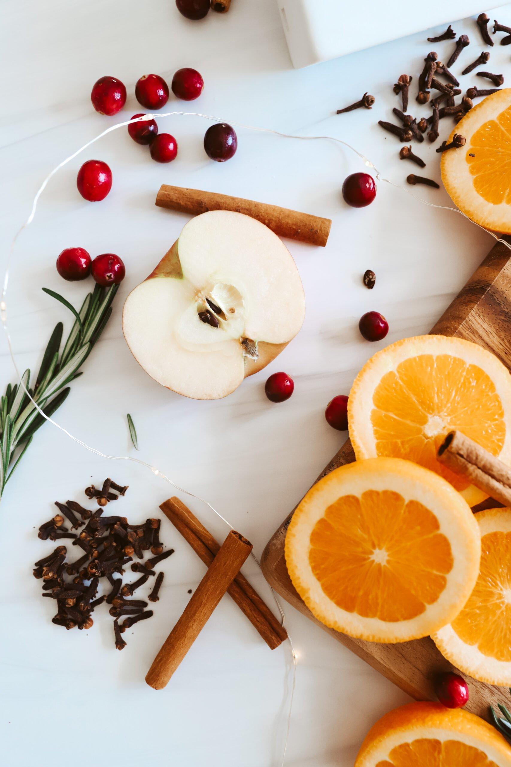 Sliced apples, oranges, cinnamon sticks, and cloves arranged beautifully on a cutting board