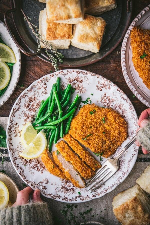 Smiling person holding a perfectly cooked, golden-brown chicken breast on a fork
