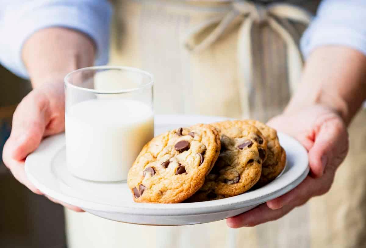 a person happily holding a plate of chocolate chip cookies
