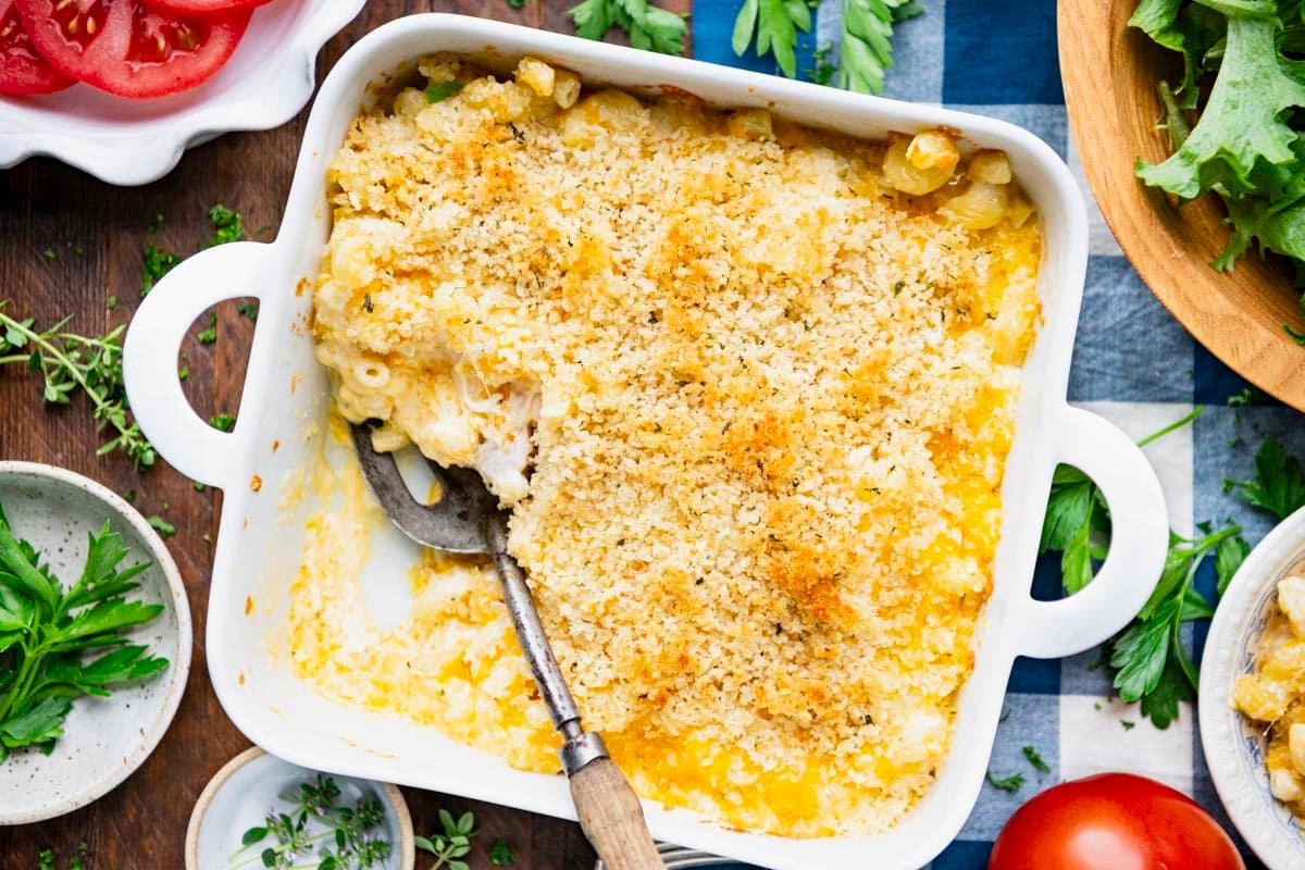 overhead shot of a table setting with a baking dish of roasted garlic and herb mac and cheese, plates, and serving utensils