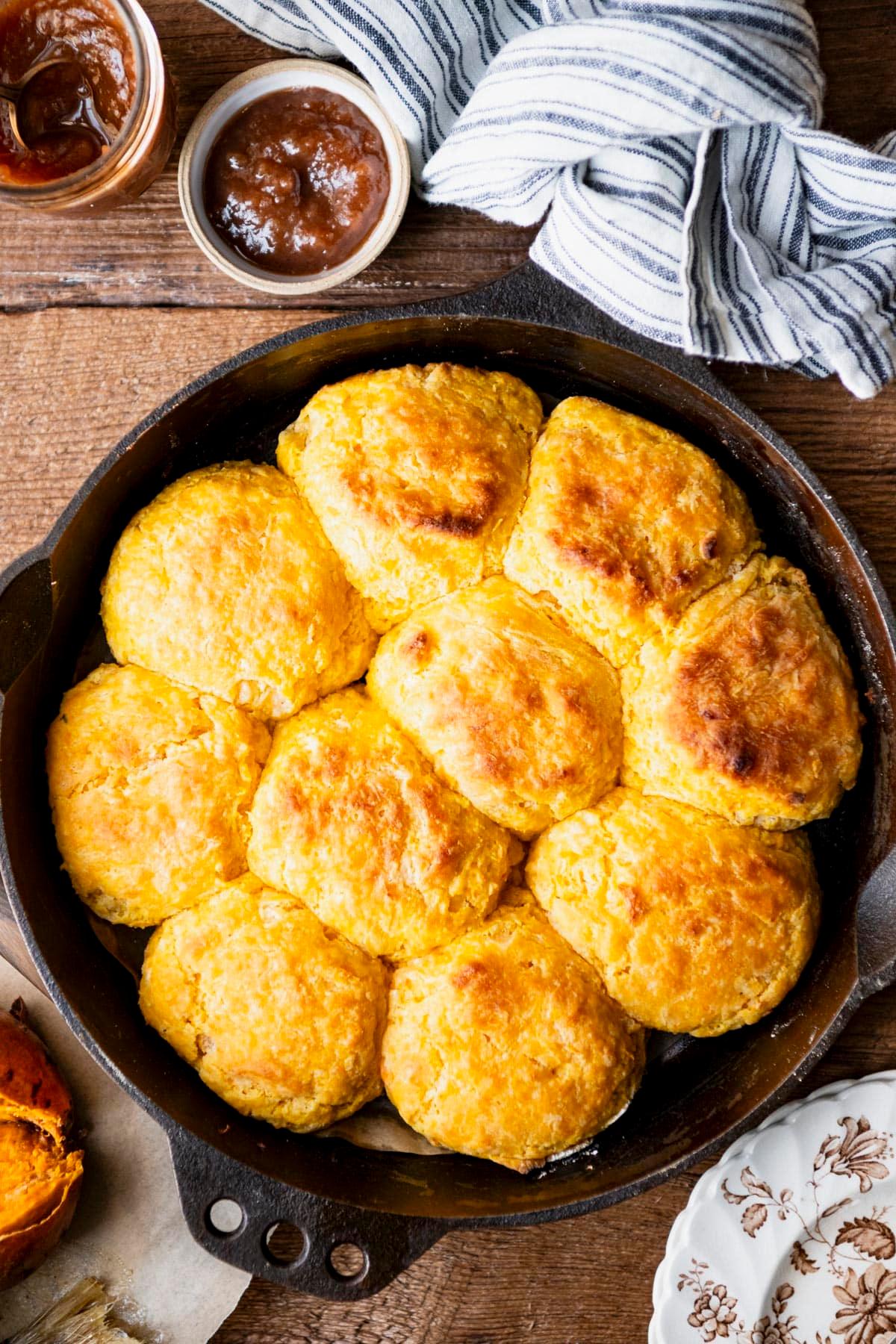 overhead shot of a basket of sweet potato biscuits next to a Thanksgiving dinner spread