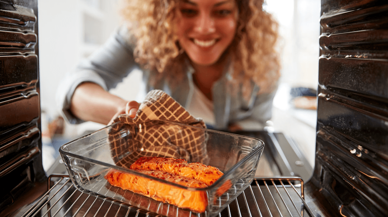 woman looking tired in a kitchen, holding a salmon fillet