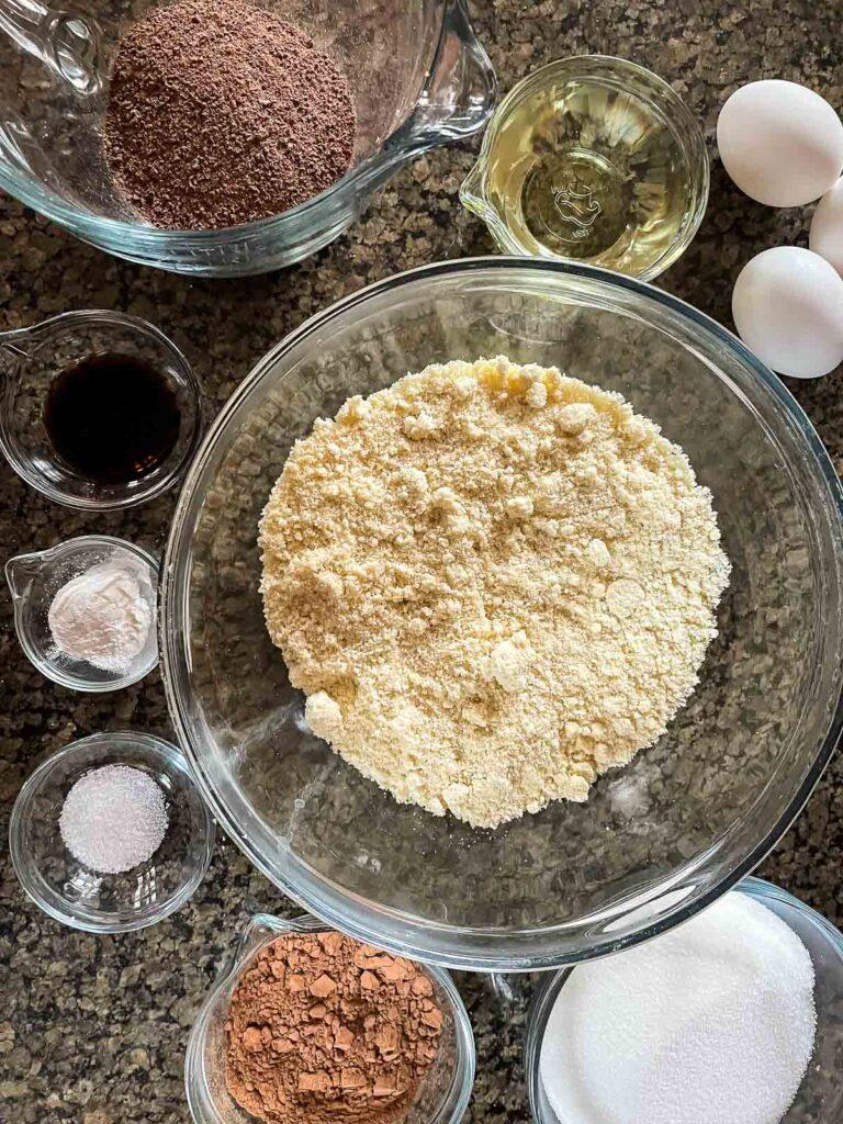A bowl of almond flour next to a bowl of cocoa powder, highlighting the key ingredients for a moist cake.