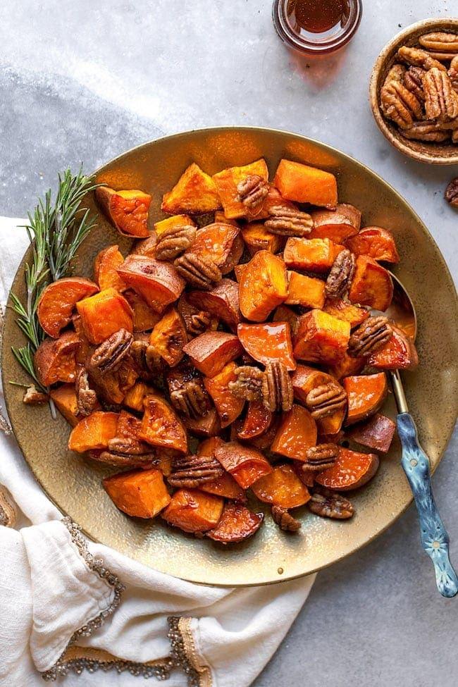 Ingredients for maple glazed sweet potato bites laid out on a wooden cutting board: diced sweet potatoes, maple syrup, cinnamon, olive oil, and fresh thyme sprigs.