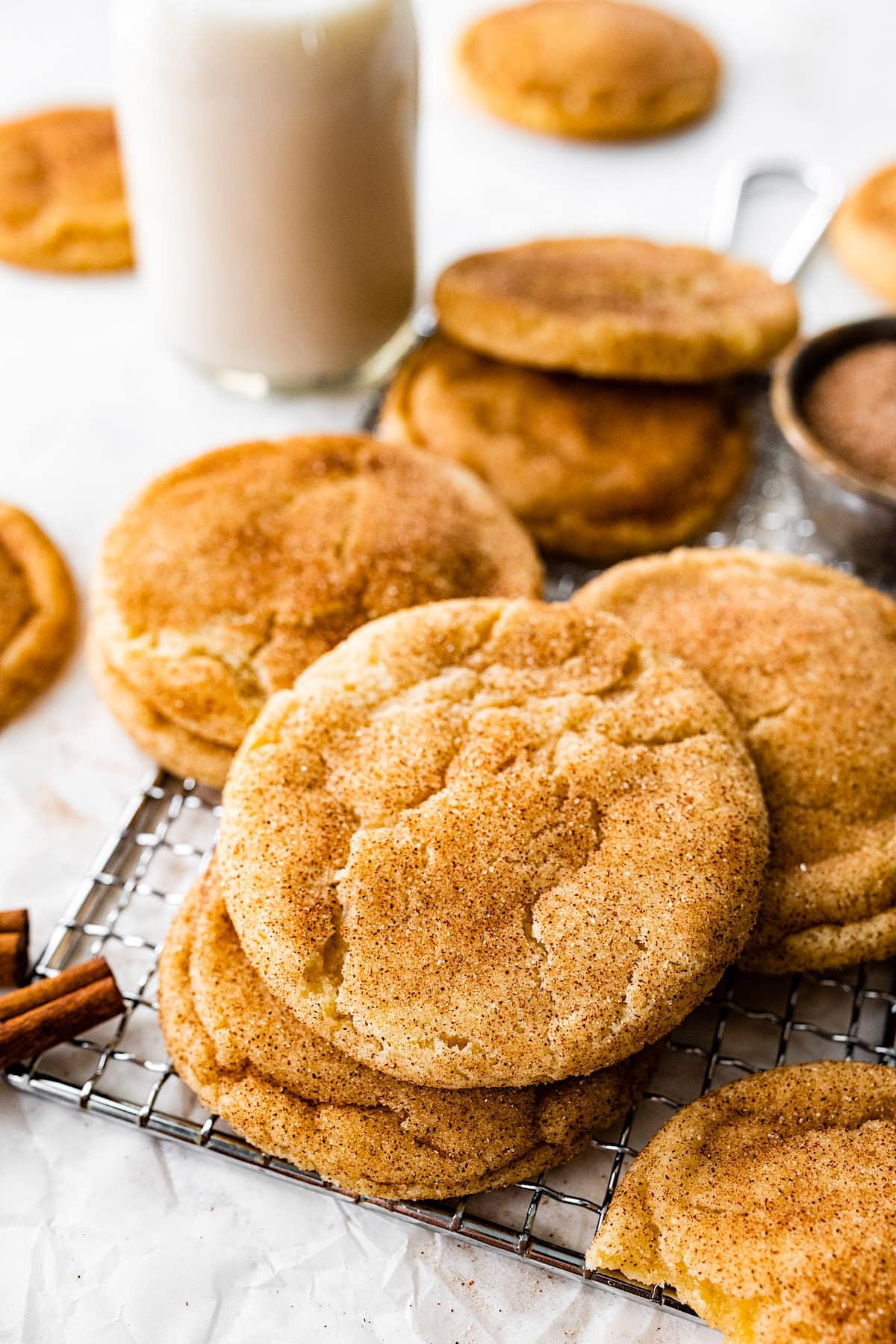 Warm snickerdoodle cookies on a cooling rack, dusted with cinnamon sugar, with a glass of milk