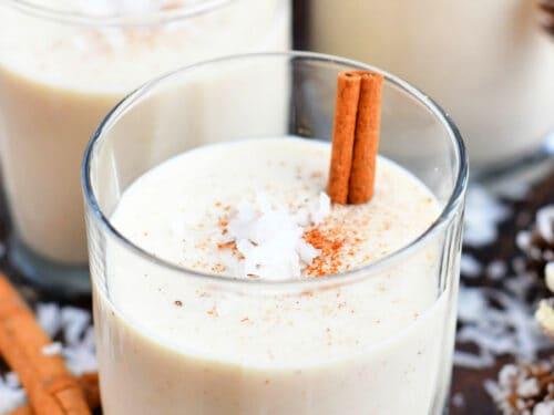 Warm, festive holiday scene with family and friends laughing, some holding small glasses of Coquito