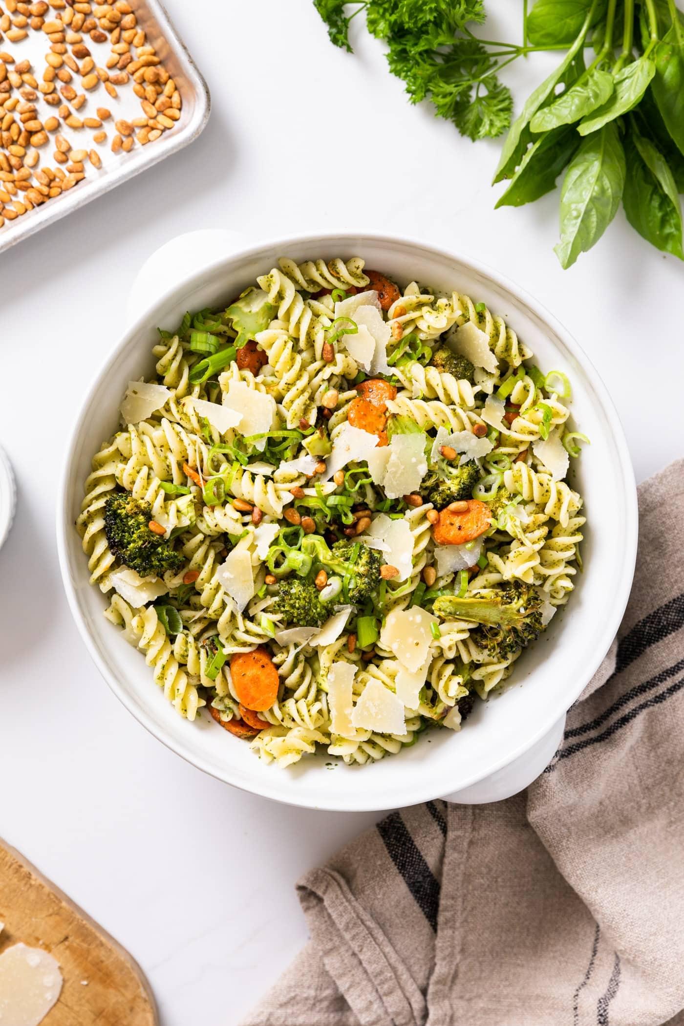 A variety of fresh herbs and spices arranged around a bowl of pasta salad.