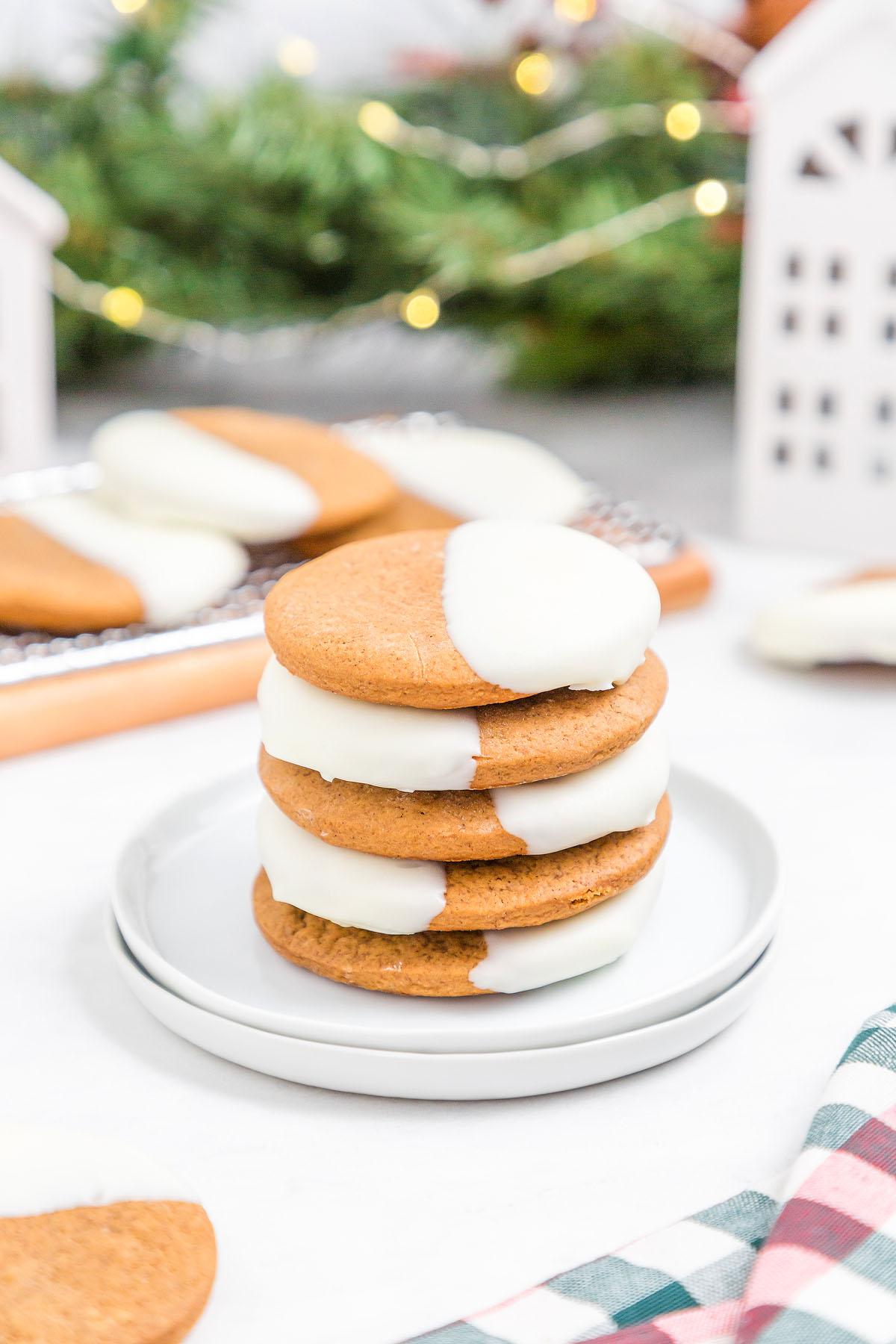 stack of white chocolate dipped gingerbread cookies on a festive plate with holiday decor in the background