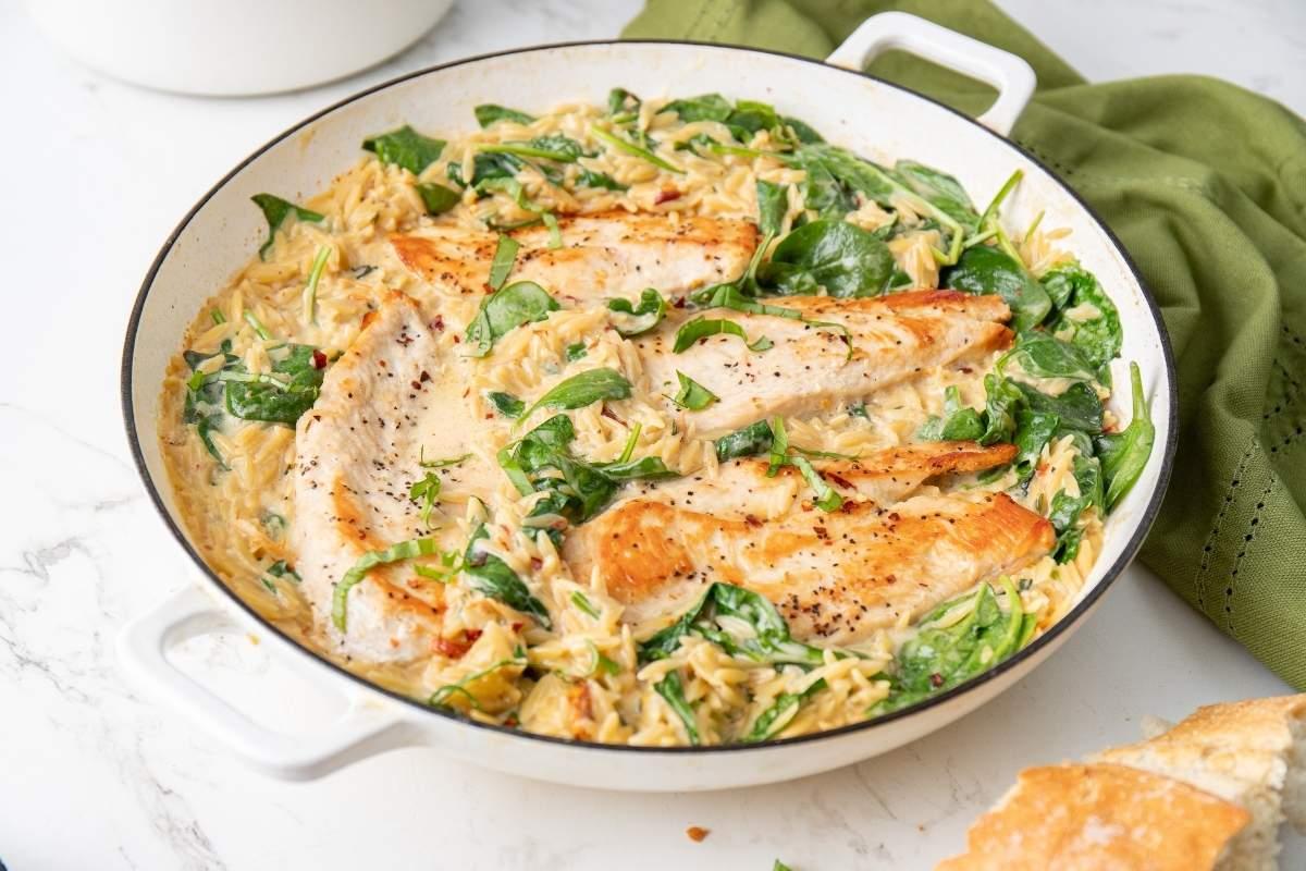 Serving of creamy Tuscan chicken orzo in a ceramic bowl, garnished with fresh basil leaves