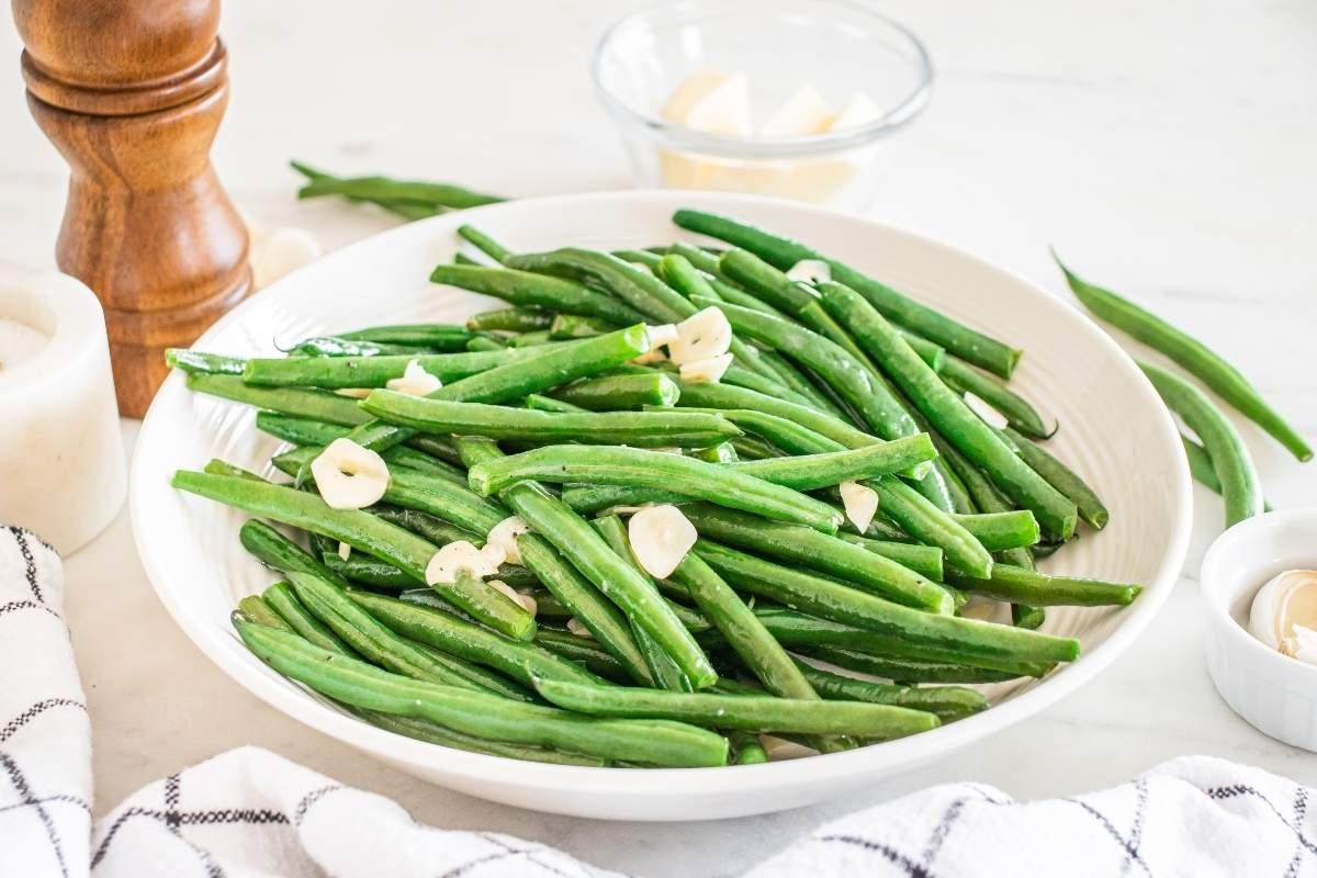 fresh green beans, garlic cloves, and olive oil on a wooden cutting board