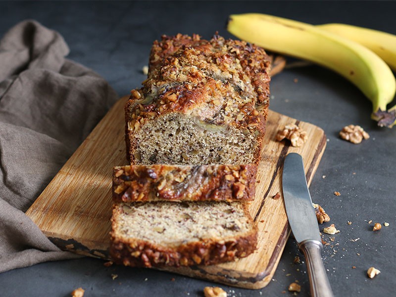 freshly baked banana bread loaf on a cooling rack with toasted walnuts on top, cozy kitchen background