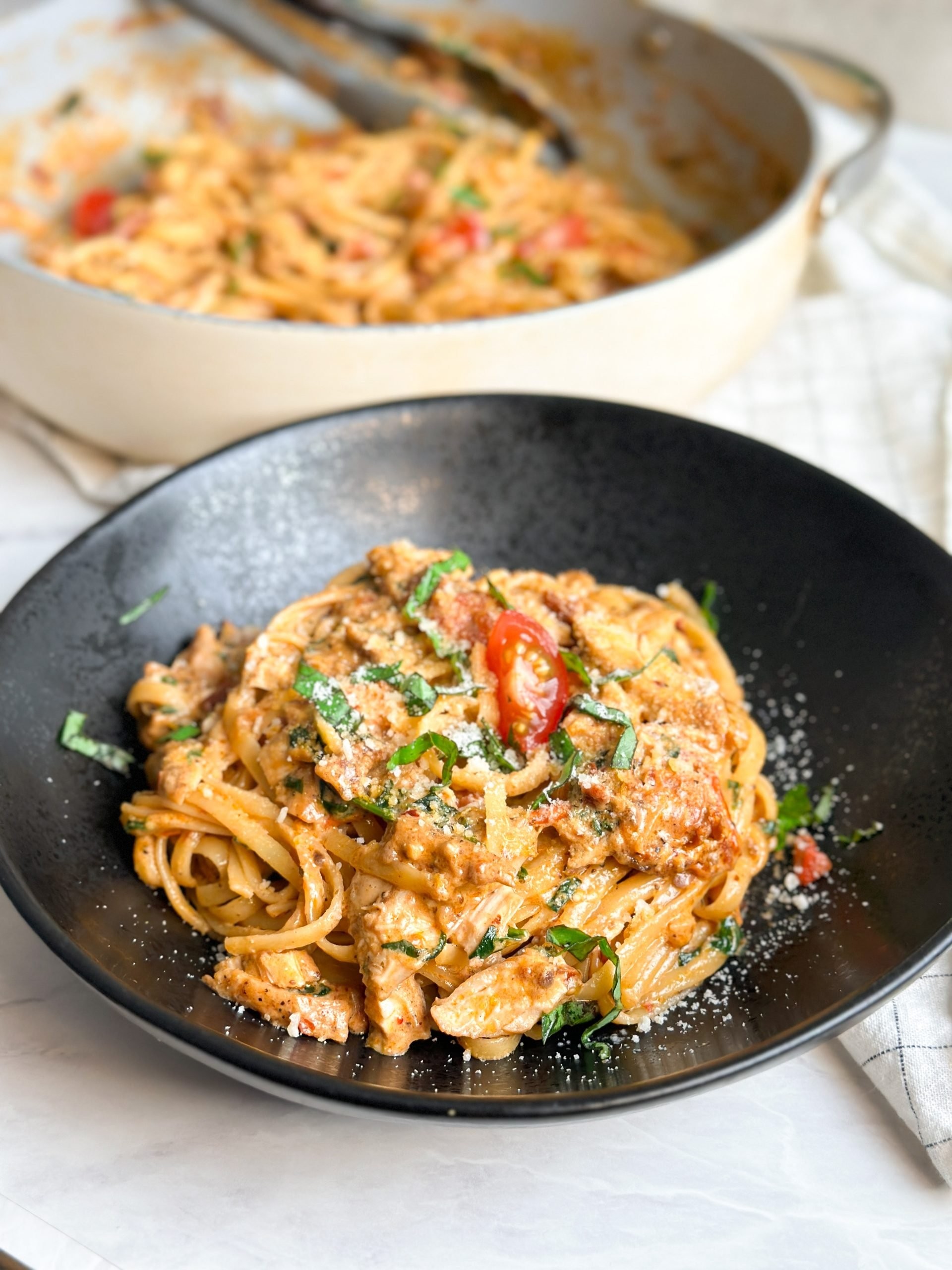 Creamy Tuscan chicken in a skillet, garnished with fresh basil and served over pasta