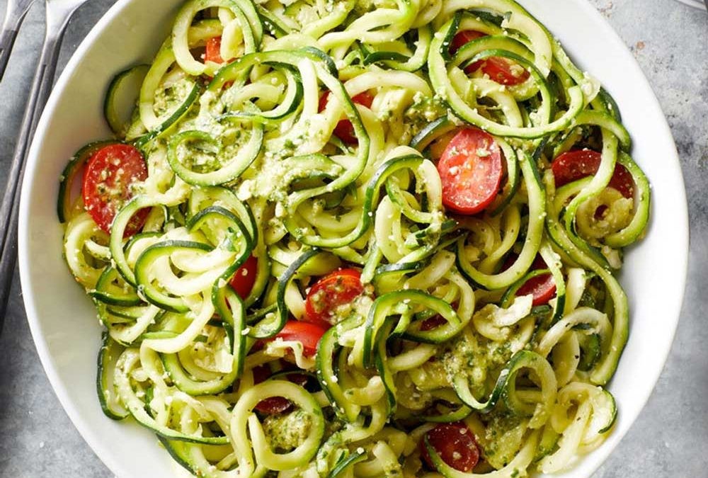 bowl of fresh zucchini noodles with garlic oil and cherry tomatoes, garnished with basil