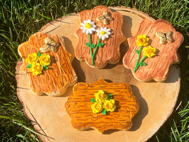 Assortment of hand-painted butter cookies with delicate floral designs on a rustic wooden board, soft lighting