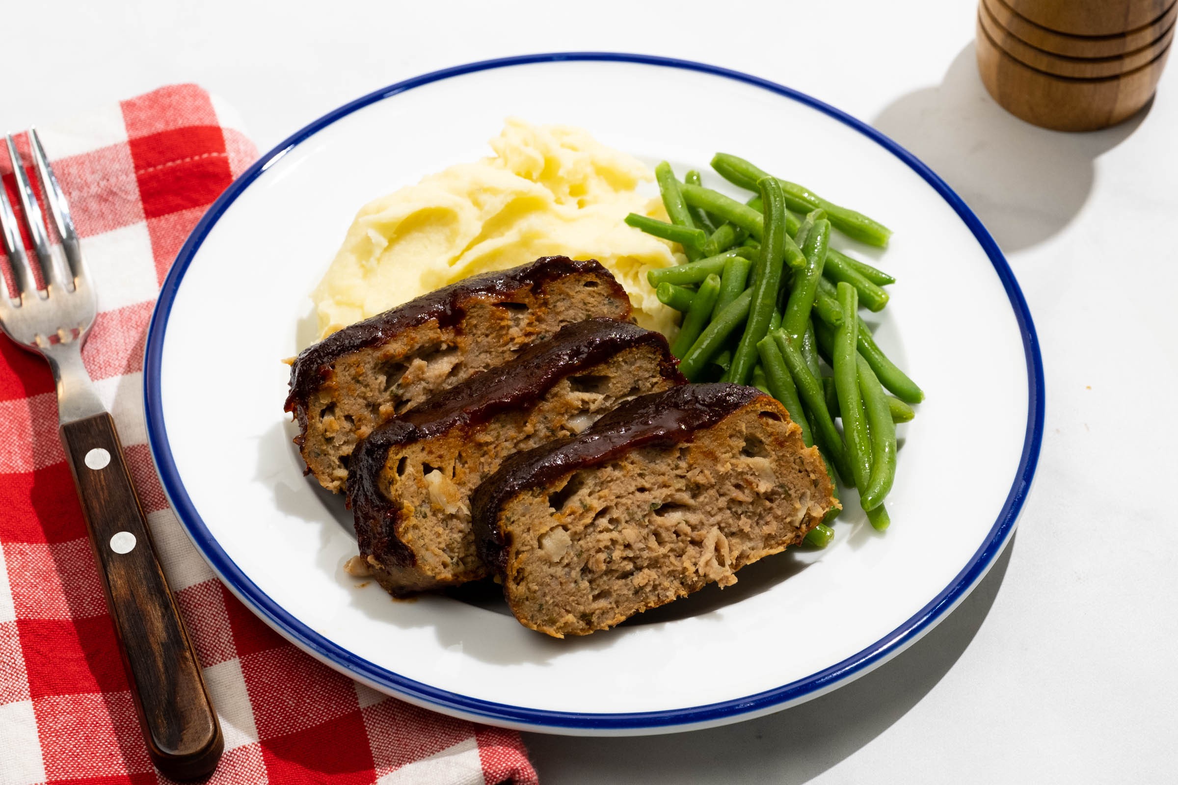 Gourmet smoky herb meatloaf sliced on a cutting board with mashed potatoes and green beans