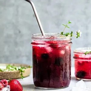 a vibrant Berry Thyme Treasure Smoothie in a clear glass, garnished with fresh berries and thyme sprigs