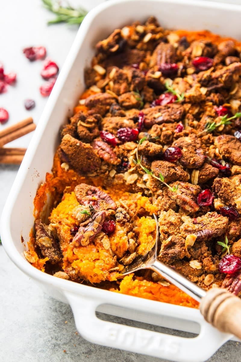 Vibrant roasted sweet potato casserole with golden brown pecan topping on a rustic wooden table, holiday setting