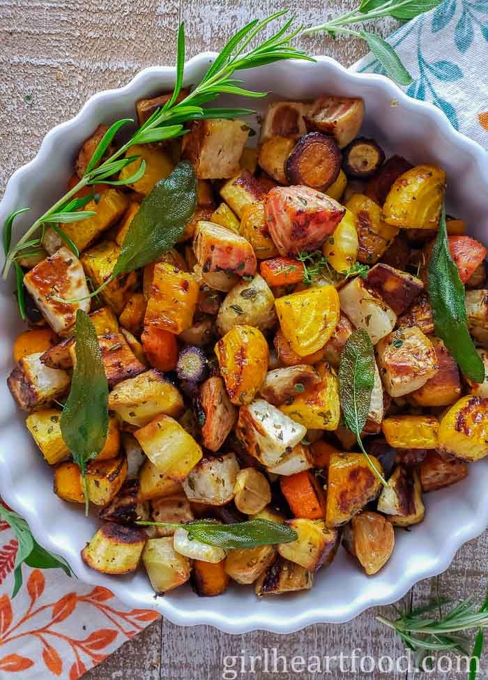 Close-up of vibrant, golden-brown roasted root vegetables drizzled with bright green herb oil on a rustic wooden board